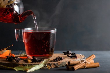 Nalewanie herbaty z hibiskusa do szklanki z dzbaneczka. Szklanka stoi na plastrze drewna.
