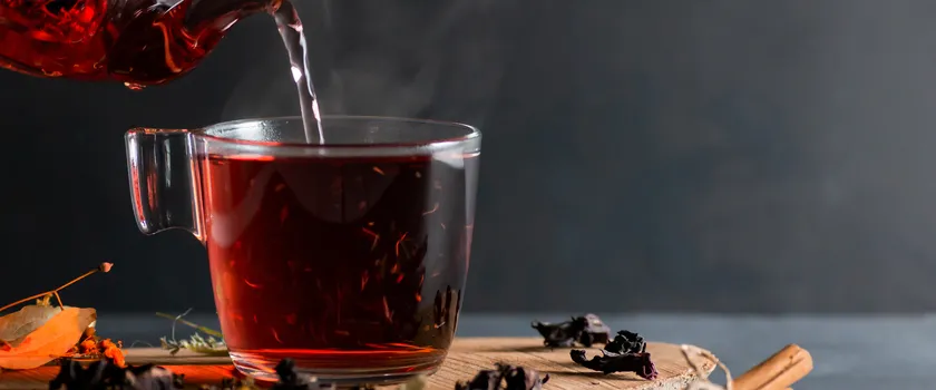 Nalewanie herbaty z hibiskusa do szklanki z dzbaneczka. Szklanka stoi na plastrze drewna.