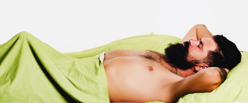 mężczyzna z erekcją leży w łóżku pod zieloną pościelą na białym tle