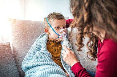 Kobieta z synem robi inhalację z nebulizatorem w domu. Dziecko cierpiące na choroby układu oddechowego.
