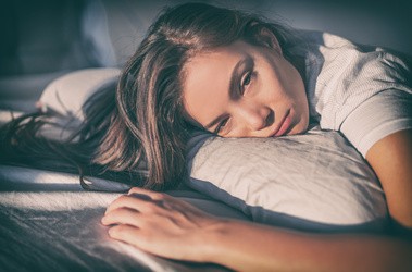 Zmęczona kobieta leżąca na łóżku i nie mogąca zasnąć ponownie.