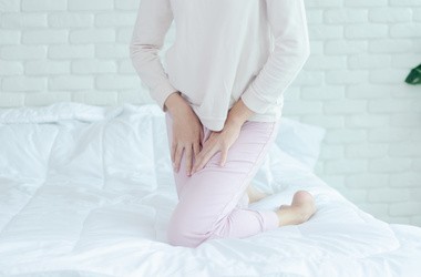 Kobieta w różowym dresie odczuwa dyskomfort w strefie intymnej.