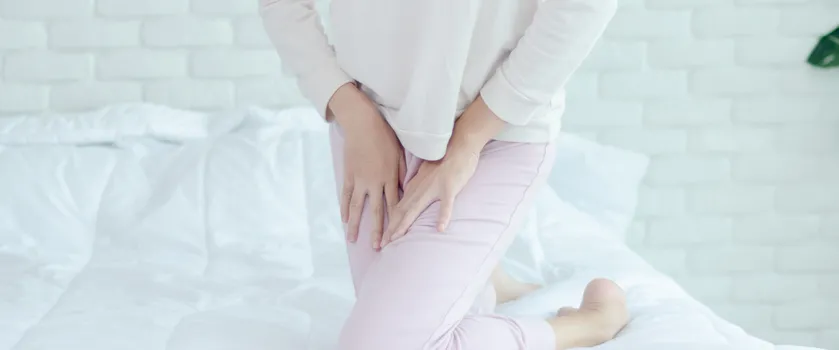 Kobieta w różowym dresie odczuwa dyskomfort w strefie intymnej.