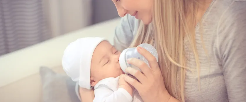 Uśmiechnięta kobieta o blond włosach karmi butelką dziecko