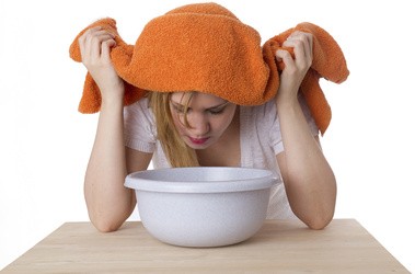 młoda kobieta z ręcznikiem na głowie robi inhalacje na zatoki nad miską